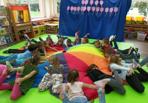 Dzieci leżące w kole podczas zabawy z chustą animacyjną.